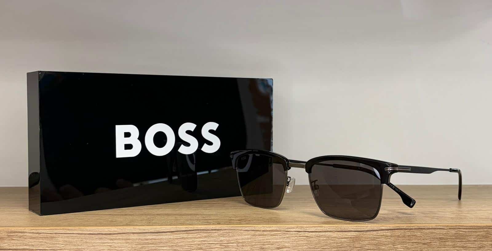 Lunettes de soleil BOSS noires sur bois avec boîte à logo BOSS blanc.