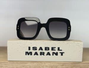 Lunettes de soleil Isabel Marant noires à monture carrée posées sur un bloc gravé, design élégant et verres dégradés.